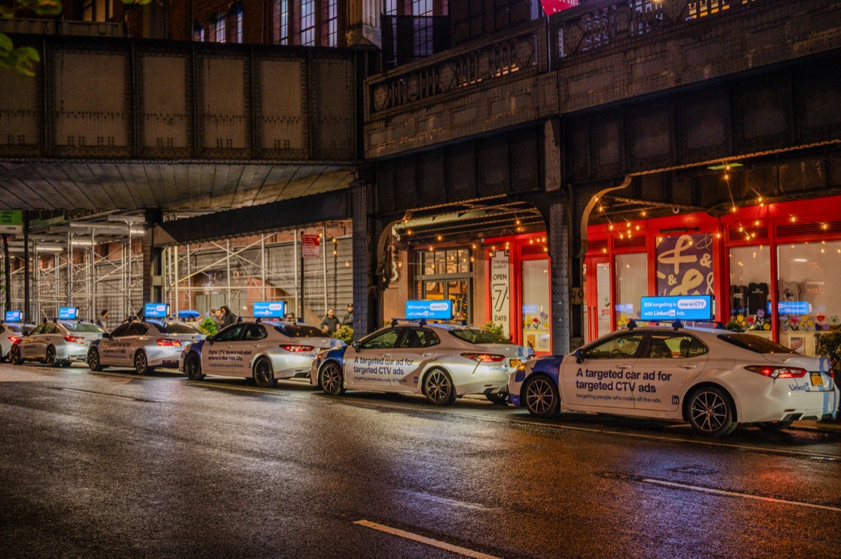 Fleet of NYC taxis with coordinated digital wrap advertising campaign driving through Manhattan streets creating a swarm branding effect
